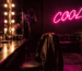 Dark scene with a glowing magenta neon sign reading COOL