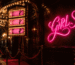 Dark scene with a glowing burlesque pink neon sign reading GIRLS
