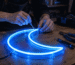 Close-up of hands installing a glowing blue neon sign in a dim room