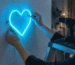 Hands mounting a blue neon heart sign on a wall with drill, screws and spirit level