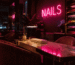 Dark scene with a glowing hot pink neon sign reading NAILS