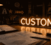 Dark scene with a glowing warm white neon sign reading CUSTOM