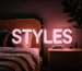 Dark scene with a glowing blush pink neon sign reading STYLES