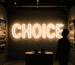 Dark scene with a glowing warm white neon sign reading CHOICE