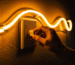 Close-up of hands working with a glowing amber neon sign in a dim room