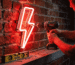 Close-up of hands working with a glowing red neon sign in a dim room