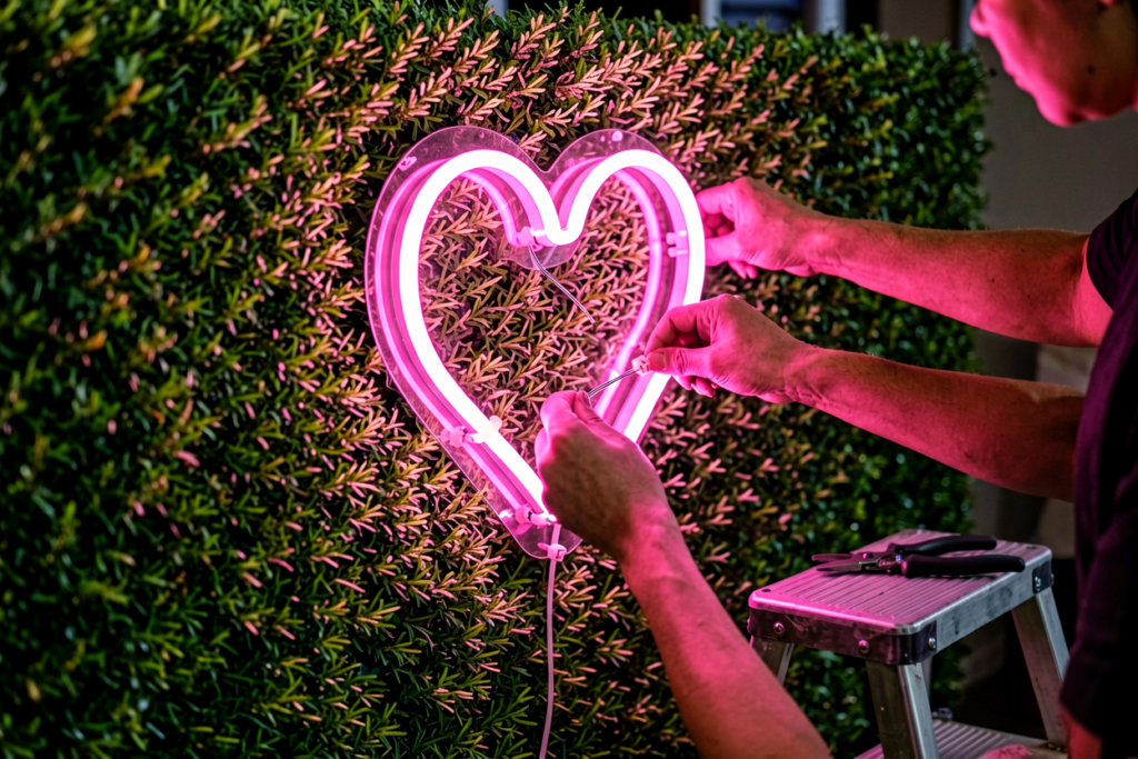 Close-up of hands working with a glowing pink neon sign in a dim room