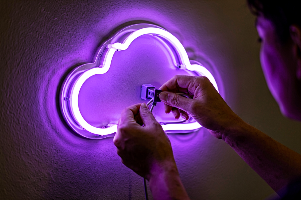 Close-up of hands working with a glowing purple neon sign in a dim room