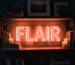 Dark scene with a glowing coral neon sign reading FLAIR