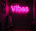 Dark scene with a glowing hot pink neon sign reading Vibes